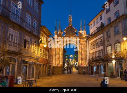 Braga, PORTUGAL - 25. Juni 2022: Menschen rund um den beleuchteten Arco da Porta Nova in Braga bei Dämmerung/blauer Stunde. Stockfoto