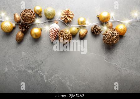 Flach auf Weihnachtsschmuck aus Gold und gelb Kegel, Kugeln aus Glas und Licht Girlande auf Tisch aus Stein. Platz für Text. Stockfoto