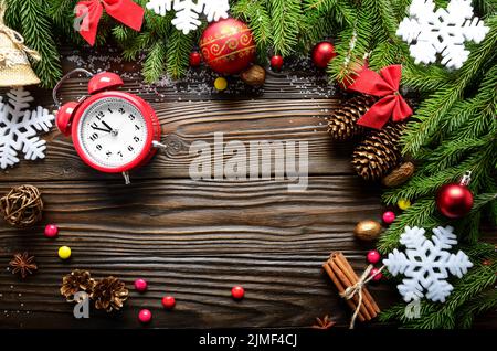 Weihnachtlicher Hintergrund von Fichtenzweigen mit Tannenzapfen und Beeren und Wecker auf Holztisch mit Kopierraum Stockfoto