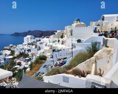 Oia, Griechenland - 22. Juni 2022: Nicht identifizierte Menschen in einer engen Straße und schöner Blick über die Stadt auf der Insel Santorini Stockfoto