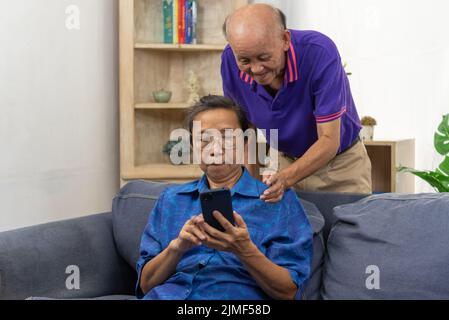 Ein asiatischer Senior hält zu Hause auf dem Sofa eine mobile Smartphone-Kommunikation online und Internet-Videoanruf ab. Stockfoto