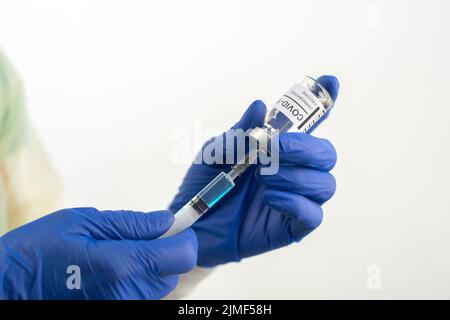 Der Arzt hält Schutzhandschuhe bereit, die die Spritze für die Injektion des Coronavirus-Impfstoffs vorbereiten Stockfoto