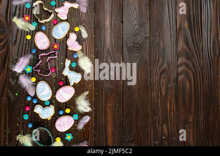 Zuckerstreuseln, Süßigkeiten, Federn, Ausstechformen, Ostergarnklätzchen in Form von Ei-Huhn und Kaninchen auf Holztisch-BA Stockfoto