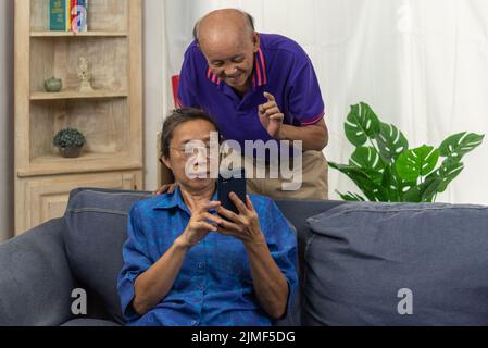 Ein asiatischer Senior hält zu Hause auf dem Sofa eine mobile Smartphone-Kommunikation online und Internet-Videoanruf ab. Stockfoto