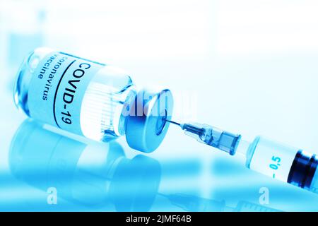 Blaues Fläschchen aus getöntem Glas mit Etikett für Coronavirus-Impfstoff und Nahaufnahme der Spritze Stockfoto