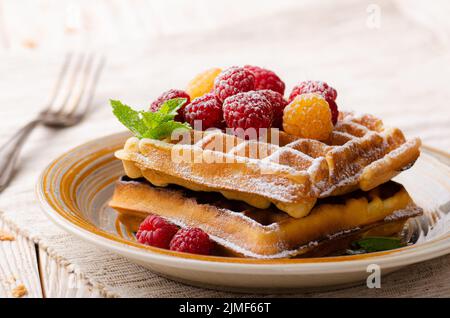 Belgische Waffeln serviert mit Himbeeren und Minzblatt bestäubt Puderzucker auf weißem Holzküchentisch Stockfoto