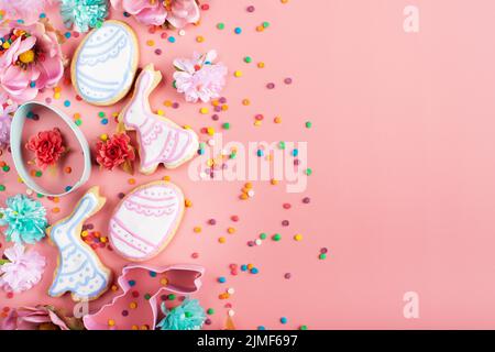 Zuckerstreuseln, Ausstechformen, Ostergarnierte Kekse in Form von Ei und Kaninchen auf rosa Hintergrund. Flaches Lay-Modell mit Kopie Stockfoto