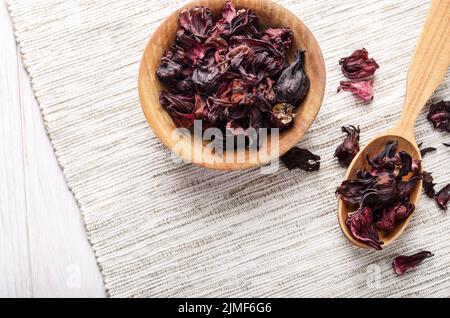 Ansicht von oben an der hölzernen Schüssel und Löffel von trockenen Hibiscus Blüten auf Leinen Hintergrund Stockfoto