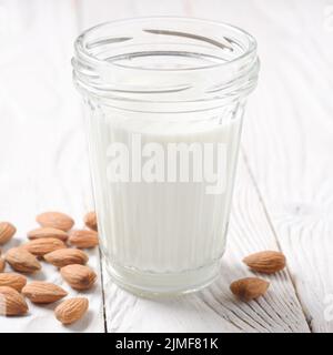 Milch oder Joghurt in Mason jar auf weissem Holztisch mit Mandeln beiseite Stockfoto