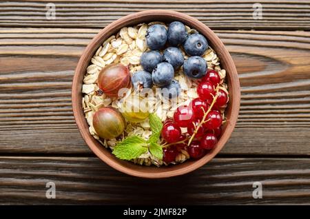 Flach auf Hafer in Ton Schüssel mit Beeren auf hölzernen Tisch Stockfoto