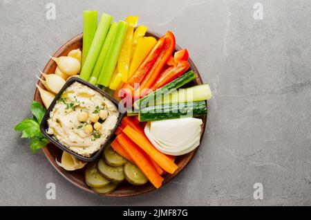 Flacher Laienblick auf die mit Kichererbsen und Olivenöl bestockte Gemüsesummus-Tauchform Stockfoto