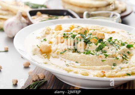 Frisch hausgemachter Hummus in Tonschale mit Olivenöl, Kichererbsen und gehackten grünen Korianderblättern auf Steintisch serviert mit Witz gekrönt Stockfoto