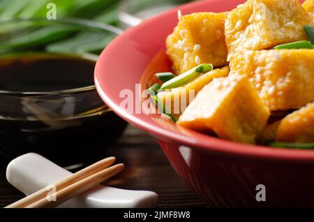 Nahaufnahme von knusprig gebratenen Tofu-Stücken mit Schnittlauch und Sesam in Tonschale Stockfoto