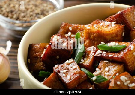 Nahaufnahme von knusprig gebratenen Tofu-Stücken mit Schnittlauch und Sesam in Tonschale Stockfoto