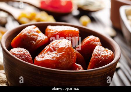 Getrocknete Aprikosen in Tonschüssel auf Holzküchentisch Hintergrund für das Essen Stockfoto