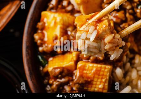 Traditionelles chinesisches Essen Mapo Tofu Gericht mit Schweinefleisch und gedünstetem Reis in Essstäbchen gehalten Stockfoto