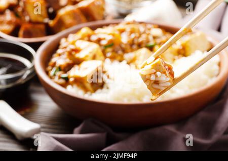 Traditionelles chinesisches Essen Mapo Tofu Gericht mit Schweinefleisch und gedünstetem Reis in Essstäbchen gehalten Stockfoto