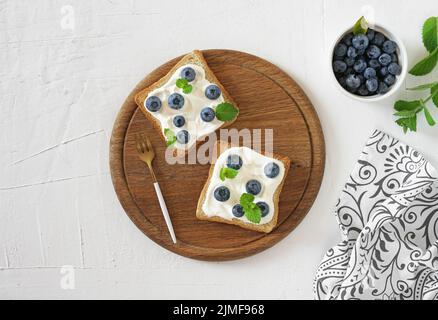 Frische, süße Brombeere, Heidelbeer-Bruschetta, Toast mit Quark, Honig in einem weißen Brett. Stockfoto