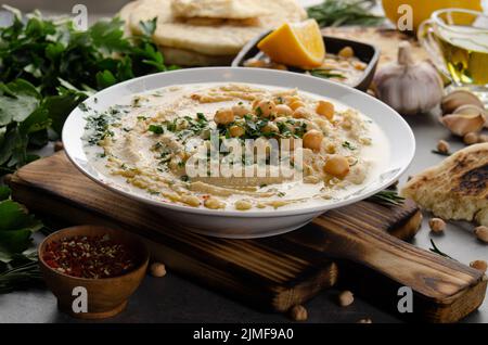 Frisch hausgemachter Hummus in Tonschale mit Olivenöl, Kichererbsen und gehackten grünen Korianderblättern auf Steintisch serviert mit Witz gekrönt Stockfoto