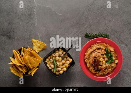 Flach legen Hummus mit sonnengetrockneten Tomaten in Tonschale mit Kichererbsen und grünen Korianderblättern auf Stein Tisch serviert mit gekrönt Stockfoto
