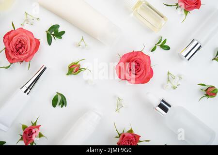 Flache Kosmetikflaschen und -Behälter mit rosa Rosen und grünem Blatthintergrund auf weißem Tisch Stockfoto