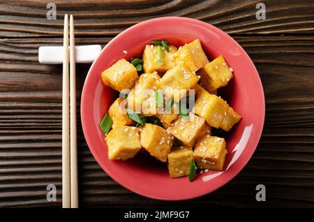 Flach legen Blick auf knusprig tief rühren gebratenen Tofu Würfel mit Schnittlauch in Tonschale auf hölzernen Küchentisch Stockfoto