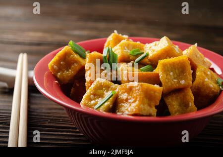 Knusprig tief gebratene Tofu-Würfel mit Schnittlauch in Tonschale auf Holztisch rühren Stockfoto