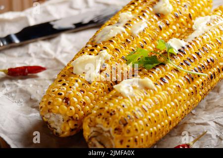 Küche Tisch mit gegrillter Zuckermais cob unter schmelzende Butter und Grüns auf Backpapier Stockfoto