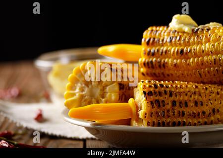 Holztisch mit tiefen gegrilltem Mais Maiskolben unter schmelzende Butter mit Kunststoffhalterung auf dunklem Hintergrund Stockfoto