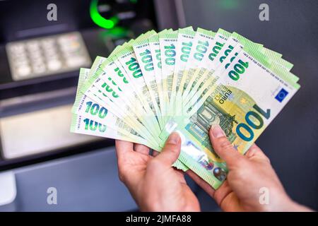 Eine Menge Geld in der Hand einer Frau. Euro-Banknoten und Geldautomat im Hintergrund. Geld in den Händen Stockfoto