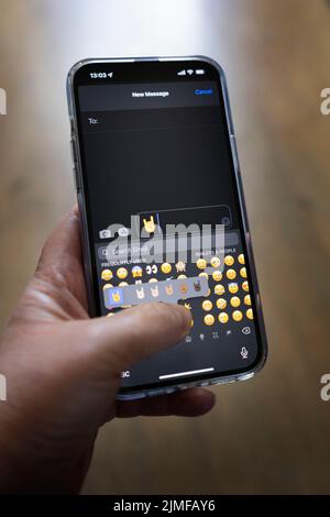 Das iPhone 13 pro max wird mit einer kaukasischen Hand gehalten, die einen Rock Fingers Emoji schreibt Stockfoto