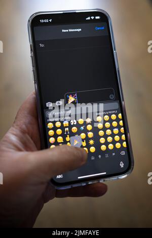 Das iPhone 13 pro max wird mit einer kaukasischen Hand gehalten, die einen Emoji schreibt Stockfoto