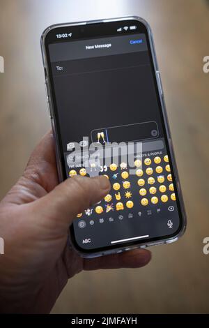 Das iPhone 13 pro max wird mit einer kaukasischen Hand gehalten, die ein klirrendes Champaign-Glas-Emoji textet Stockfoto