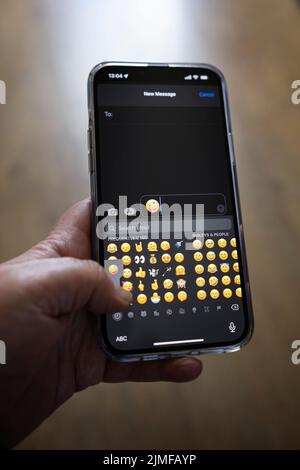 Das iPhone 13 pro max wird mit einer kaukasischen Hand gehalten, die einen Emoji schreibt Stockfoto