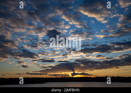 Epische rote, blaue und goldene Wolken über dem Waldsee bei Sonnenaufgang. Dramatische, farbenfrohe Wolkenlandschaft. Symmetriereflexionen auf dem Wat Stockfoto