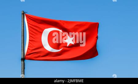 Nationalflagge der Türkei auf einem Fahnenmast im Wind auf einem Hintergrund von blauem Himmel. Stockfoto