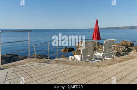 Sonnenschirm und Sonnenliegen an der Küste der Adria in der Nähe der Stadt Krk in Kroatien Stockfoto