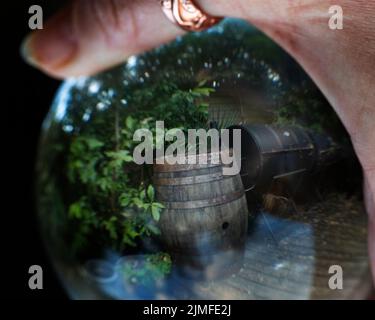 Ein Whisky-Fass aus Holz in einem Garten, der durch einen Linsenball gesehen wird, Großbritannien Stockfoto