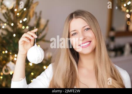 Dekoration Weihnachtsbaum und Winterferien Konzept. Glücklich lächelnde Frau hält festliche Ornament zu Hause Stockfoto