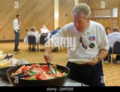 Calvert City, KY, USA. 05 August 2022. Ein nicht identifizierter Teilnehmer hilft sich selbst, Wassermelonen in der Buffetlinie zu schneiden, während Drew Williams, Vorsitzender des Exekutivkomitees der Marshall County Democratic Party (hinten links), mit Gästen beim Mike Miller Memorial Marshall County Bean Dinner 25. im Kentucky Dam Village State Resort Park spricht. Die Spendenaktion der Marshall County Democratic Party findet in der Nacht vor dem jährlichen St. Jerome Fancy Farm Picnic statt, dem traditionellen Beginn der politischen Wahlkampfsaison in Kentucky. (Kredit: Billy Suratt/Apex MediaWire über Alamy Live News) Stockfoto