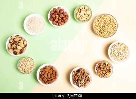 Ovaler Rahmen aus Schalen mit Getreidekörnern und Nüssen auf zweifarbigem beige-grünem Hintergrund. Diät oder Ernährung Konzept. Superfoods. Vegane Proteinquelle. Gesund Stockfoto