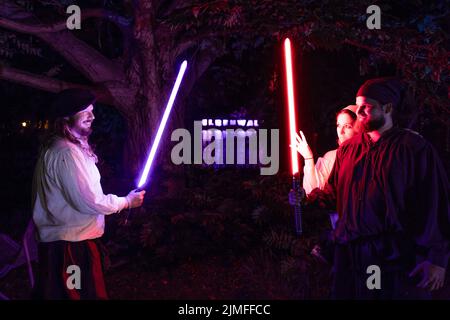 Cottbus, Deutschland. 05. August 2022. Kostümierte Besucher des Elbenwalder Festes stehen mit Lichtschwert am Ufer eines Teiches im Spreeauenpark. Das Elbenwald Festival ist ein dreitägiges Treffen für Menschen jeden Alters, die Filme, Fantasy, Spiele, Konzerte und jede Kombination von allen genießen. Quelle: Frank Hammerschmidt/dpa/Alamy Live News Stockfoto