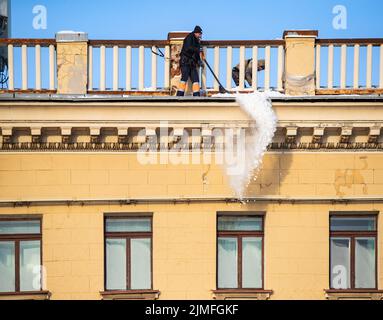 Russland, St. Petersburg, 07. Dezember 2021: Die Arbeit der Versorgungsunternehmen, um Schnee von den Dächern von Häusern zu entfernen, wirft ein Mann die sn Stockfoto