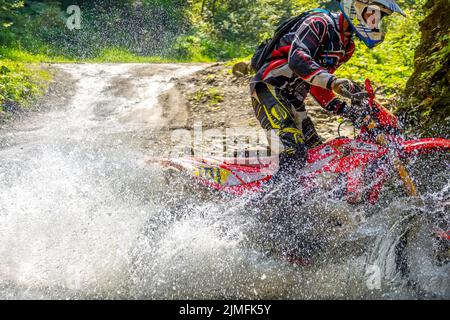 Motorrad in Wasser Spray und Athlete Enduro Stockfoto