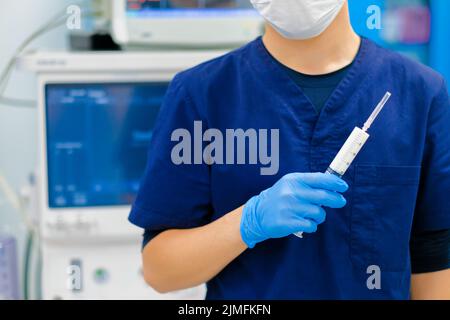 Die Hand des Arztes in einem sterilen Handschuh hält eine Spritze. Stockfoto