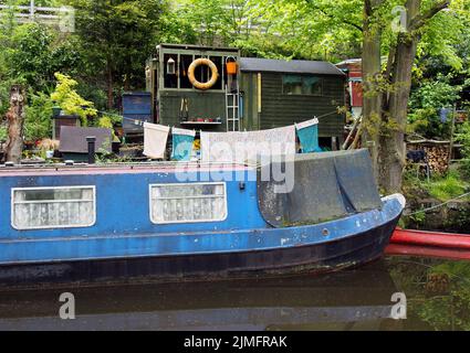 Ein altes, schmuddeliges, blaues, enges Boot, das neben Holzschuppen festgemacht ist und auf dem rochdale Kanal in der Nähe der hebdenbrücke gewaschen wird Stockfoto