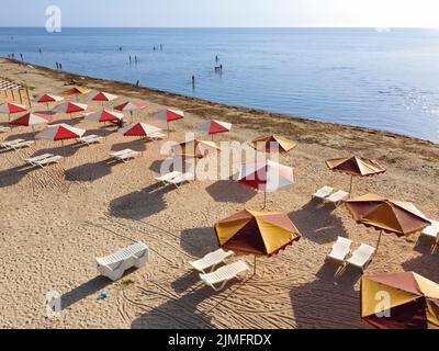 Strand mit Sonnenschirmen und schmutziges Meer, das viele Algen bringt Zum Ufer Stockfoto