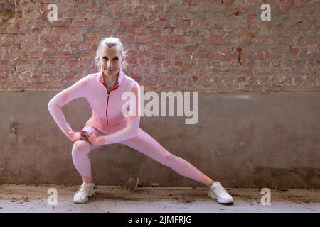 Schöne junge blonde Fitness-Frau trägt rosa Sportkleidung Stretching und Aufwärmen Beine am Morgen. Sportliche Frau, die w Stockfoto