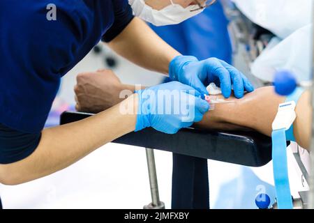 Der Arzt führt eine Tropfernadel in eine Vene im Arm des Patienten ein. Stockfoto