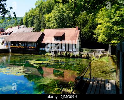 Eine malerische Aussicht auf den smaragdgrünen Blautopf-See und die historische alte Hammermühle in der Nähe des Klosters Blaubeuren in der alten romantischen deutschen Stadt Blaubeuren (Deutschland) Stockfoto